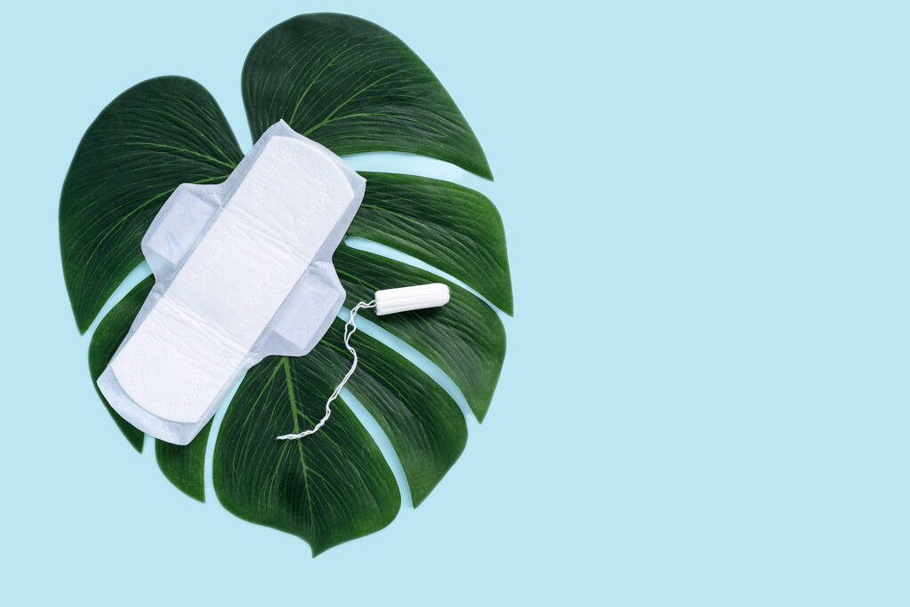 top view sanitary pads and tampon on leaf on blue background, copy space